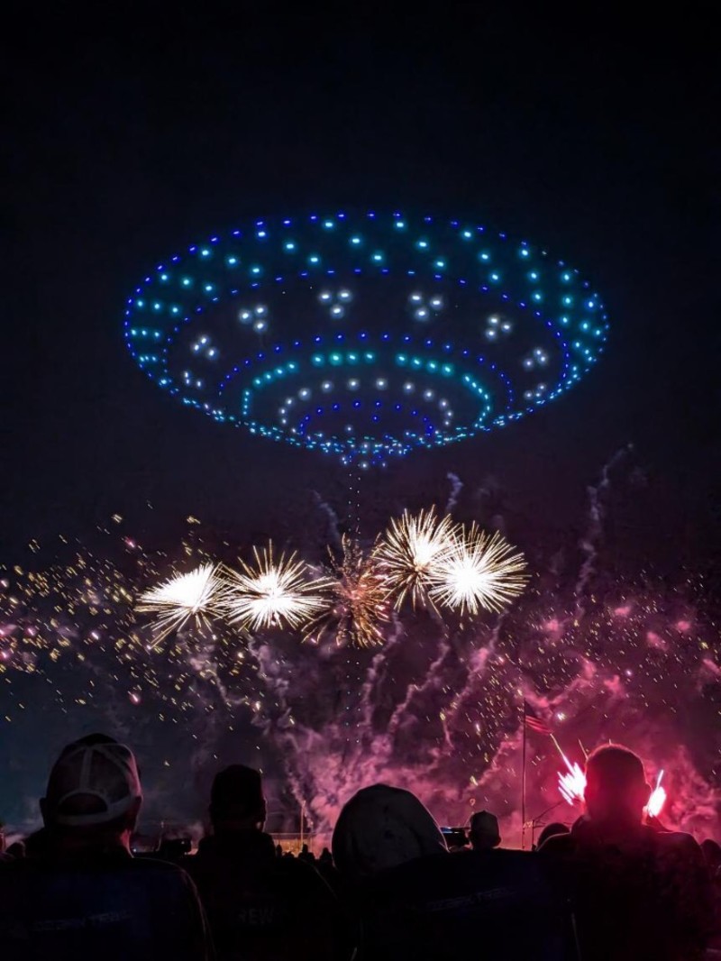 Blue drone lights forming a flying saucer above golden fireworks